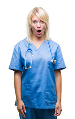 Poster - Young beautiful blonde doctor woman wearing medical uniform over isolated background afraid and shocked with surprise expression, fear and excited face.