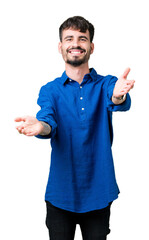 Wall Mural - Young handsome man over isolated background looking at the camera smiling with open arms for hug. Cheerful expression embracing happiness.