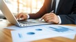 © EgonDorr - A businessman in a suit, focusing on his laptop while analyzing financial reports and data sheets in a bright office setting.