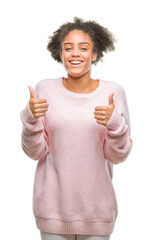 Wall Mural - Young afro american woman wearing winter sweater over isolated background success sign doing positive gesture with hand, thumbs up smiling and happy. Looking at the camera with cheerful expression