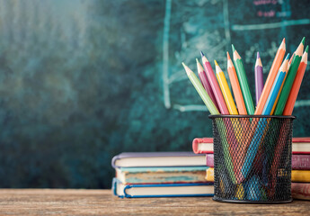 Aufkleber - Colorful pencils standing in metal holder near books on wooden table with blurred chalkboard on background, education concept