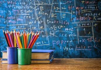 Poster - Colorful pencils in cups on a desk with books and a chalkboard background back to school concept