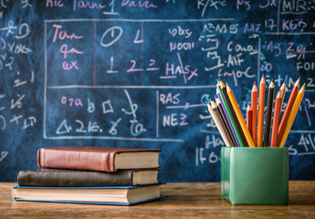 Aufkleber - Colorful pencils in a cup and a stack of books on a teacher's desk with background of a blackboard