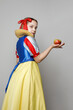 © millaf - Pretty young girl theater actress in SnowWhite costume holding apple and standing on white background