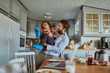 Father and son playing and laughing in kitchen during breakfast