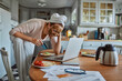 © Geber86 - Woman with face mask enjoying breakfast and coffee while working on laptop in kitchen