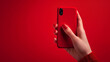 © Sana Sabina - A female hand with a red manicure holding a phone in the red case on a red background.