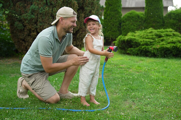 Poster - Father and his daughter watering lawn with hose in backyard, space for text