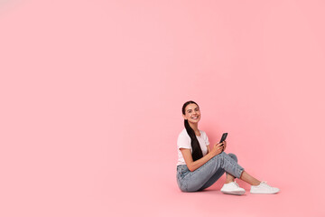 Wall Mural - Smiling woman with smartphone on pink background. Space for text