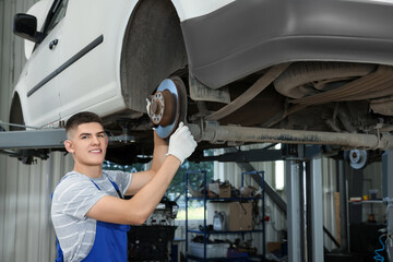 Poster - Young auto mechanic fixing lifted car at automobile repair shop