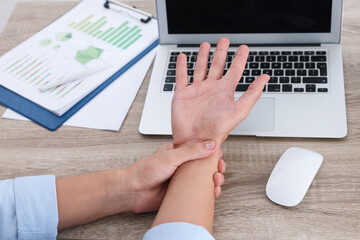 Poster - Man suffering from pain in wrist while working on laptop at wooden table, closeup. Carpal tunnel syndrome