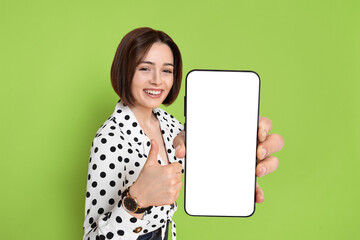 Wall Mural - Happy woman showing mobile phone with blank screen on green background. Mockup for design