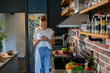 © Geber86 - Smiling young woman using smartphone in modern kitchen