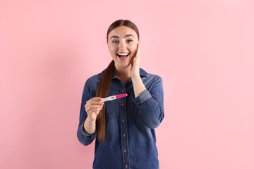 Canvas Print - Happy woman holding pregnancy test on pink background