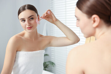 Wall Mural - Beautiful young woman doing facial massage with roller near mirror at home