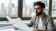 © LarisaM - Bearded architect in glasses intently studying blueprints in a modern office with large windows overlooking a cityscape.