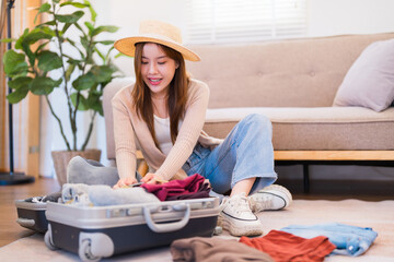 A young woman is sitting on the floor, securing the straps in her packed suitcase with a focused expression, preparing for her trip while wearing a hat and casual clothes