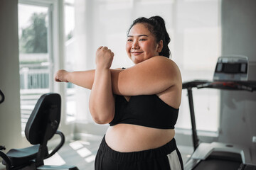 Plus size Asian woman exercises in gym. Beautiful overweight woman in sportswear smiling and happy in fitness. concept of body positive, self-acceptance, weight loss.