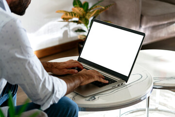 Young business man using computer laptop in front of an blank white computer screen in his home living room. Photo ready for mockup.