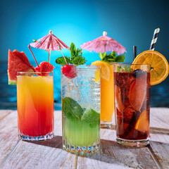 Wall Mural - Summer cocktails, focusing on a close-up shot with vibrant colors. The image includes variety of cocktails in clear, well-lit glasses, garnished with fresh fruits, herbs.