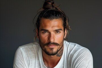 Handsome man with Top Knot hair style in casual white shirt gazing intensely at the camera against dark background. Concepts include self-confidence, attractiveness, and individuality.