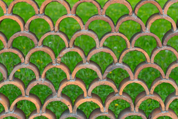 Decorative fence made of semicircular bricks, arranged in a staggered pattern, creating a unique design with gaps between the elements.