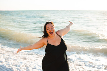 Laughing overweight woman 30 - 35 year old wearing black dress at black over sea outdoor. Happiness. Body positive.