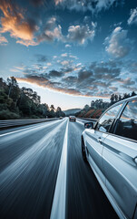 A car is driving down a highway with a beautiful blue sky in the background. The sky is filled with clouds, giving the scene a serene and peaceful atmosphere