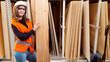 © Grispb - Woman builder. Board in hands of girl carpenter. Woman repairman shows parquet sample. Work in wood processing industry. Female employee of furniture factory. Lady furniture maker in orange vest