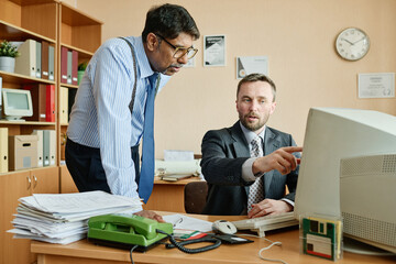 Aufkleber - Two business professionals collaborating on work tasks in office setting, with documents and computer visible on desk. One man pointing at screen, other listening intently