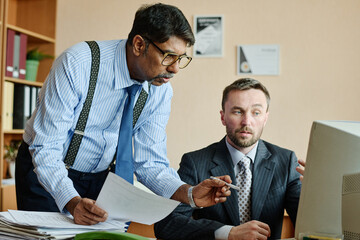 Aufkleber - Two business professionals are discussing strategies while looking at documents and computer. Office environment with shelves and office supplies in background