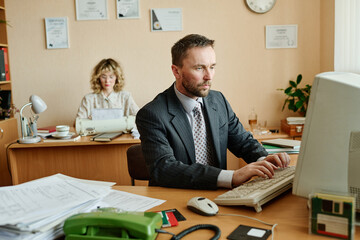 Poster - Man and woman working in office setting with desks, documents, and various office equipment. Man focused on computer task, while woman uses a typewriter in background