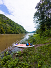 A vibrant and colorful paddle board rests patiently on the sandy shoreline of a stunning river, basking in the bright sunlight, surrounded by the serene and picturesque beauty of natures landscape