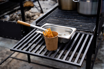 A warm, inviting cup of crispy french fries is carefully placed on a hot grill, eagerly waiting to cook to perfection, creating a delightful treat or snack that everyone can enjoy