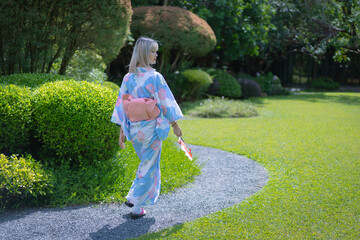 Pretty girl in a Yukata dress.  A young Asian woman wearing a traditional Japanese kimono or Yukata dress is happy relaxing in the green natural Japan park. Female portrait beauty and fashion.