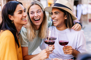 three young multiracial women having fun enjoying aperitif with red wine in a restaurant. female fri