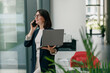 © Viktoria Kovalchuk - A businesswoman is talking on the phone while holding a laptop in a modern office
