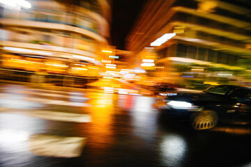 A dynamic and vibrant night cityscape featuring a fast-moving car on a wet street, with blurred motion effects from lights and reflections, capturing the energy of urban nightlife