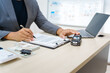 © Phushutter - Asian business professional in a formal suit works at a desk, reviewing financial charts. manage car insurance claims, analyze auto loan options, sign lease agreements for vehicle transactions.