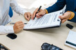 © Phushutter - A middle-aged Asian male seller in a formal suit assists a woman buyer at a desk. They finalize a vehicle lease, reviewing financial charts and signing contract agreements with a car key.