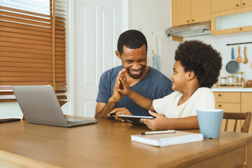 Wall Mural - Black African American Father and son high five at kitchen table after using tablet, celebrating a successful bonding moment with technology.