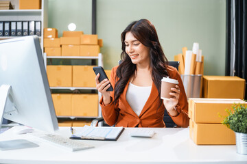 A young Asian businesswoman sits at her table, watching the computer screen.She analyzes, plans, and sells products online from home, smiling as she replies to comments and takes orders successfully.