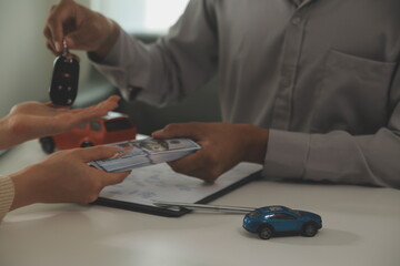 Young man receives a key from car salesman. After agreeing to a contract for rent or sale of a car at workshop, loan car, insurance, sale, buying car and finance concept.