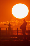 Fototapeta Big Ben -  A few individuals stand on a beach, near the ocean, beneath a big, orange sun