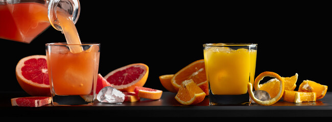 Wall Mural - Glasses of grapefruit and orange juice with ice on a black background.