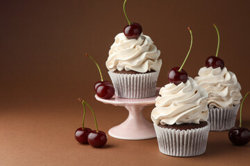 Wall Mural - Delicious cupcakes with cream and cherries on brown background, space for text