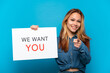 © luismolinero - Teenager girl over isolated blue background holding We Want You board and pointing to the front