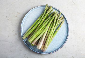 Plate with fresh green asparagus stems on light textured table, top view