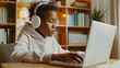 © VK Studio - A young boy with headphones working on his laptop, surrounded by books and plants, in a brightly lit, well-organized study room.