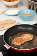 © New Africa - Cooking schnitzel in frying pan on stove, closeup